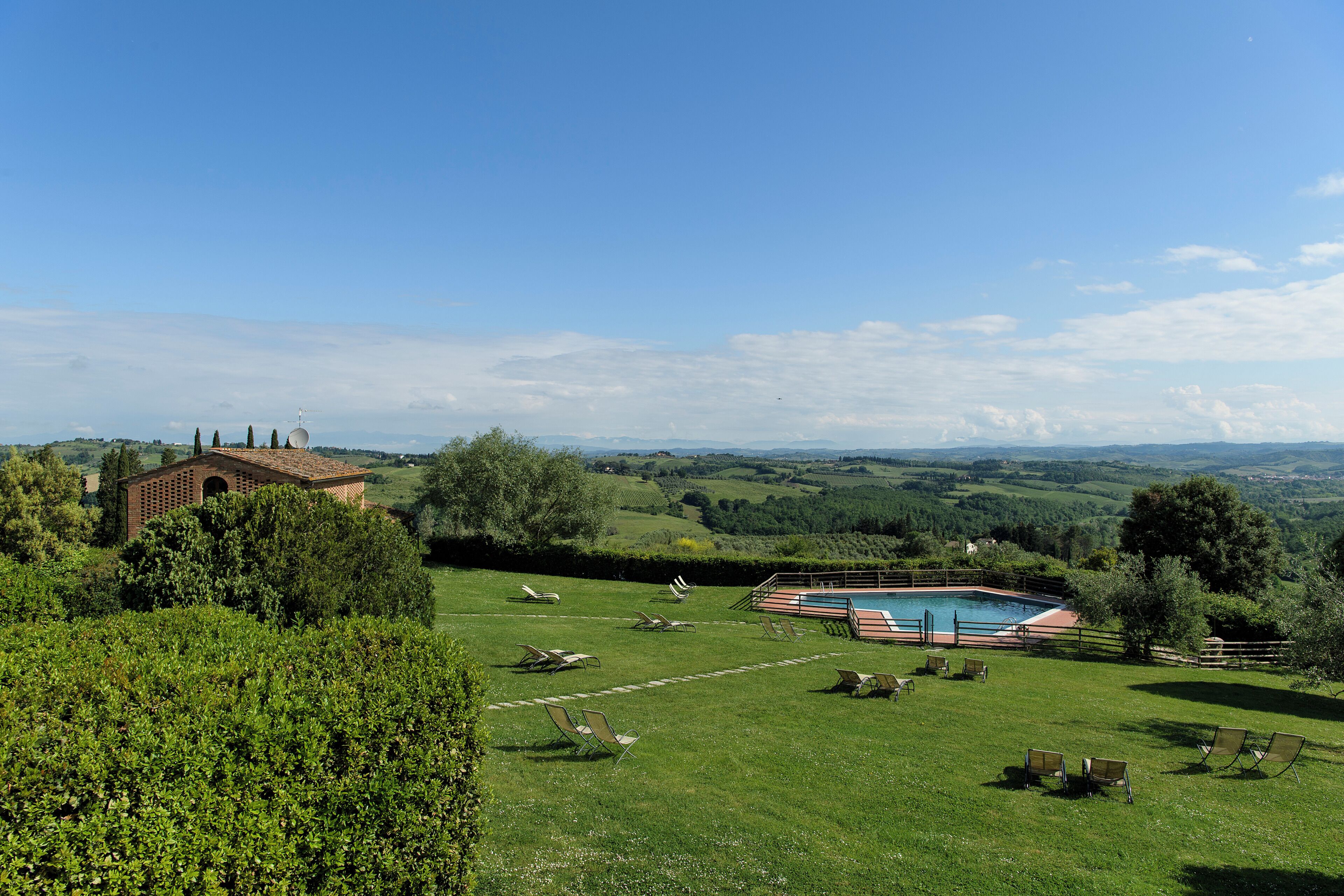 A pool area with lounge chairs, a brick building, and a view of rolling hills.