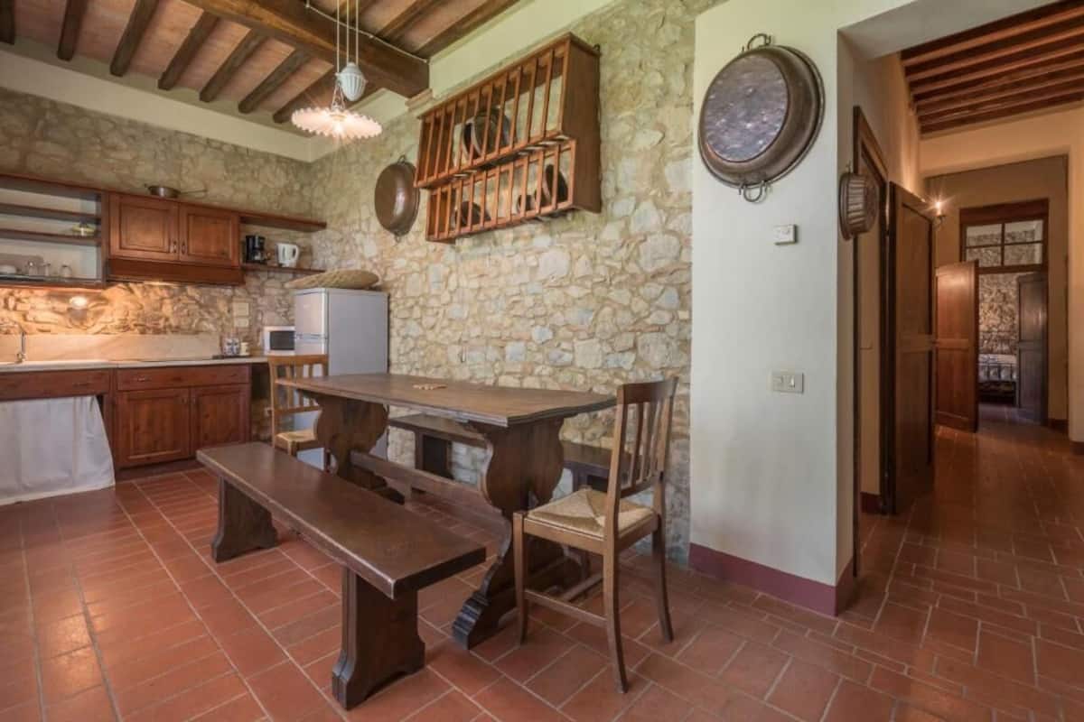 A rustic kitchen with stone walls, wooden cabinets, a large wooden table, and a bench.