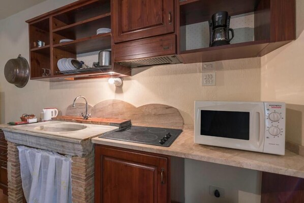 Une cuisine équipée d’un évier en pierre, d’une cuisinière, d’un four à micro-ondes, de meubles de rangement en bois et d’une casserole suspendue.