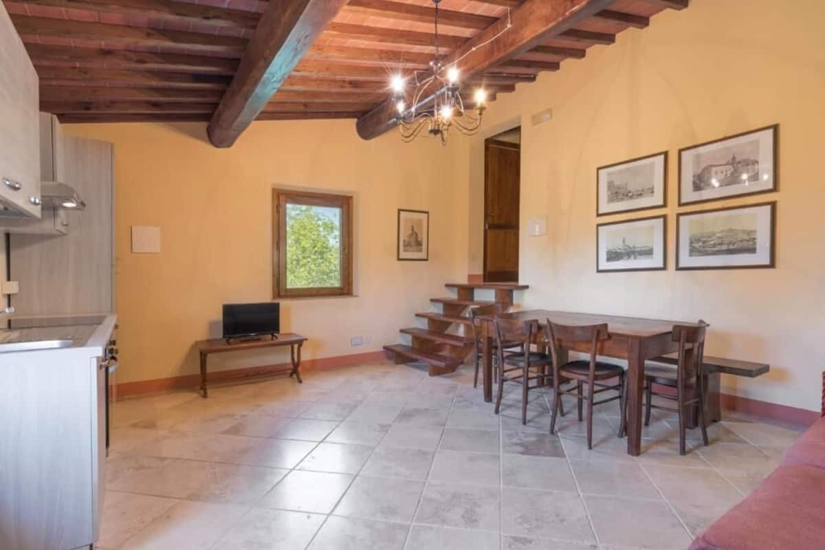 A dining area with a wooden table and chairs, a television, and a staircase leading to another level.
