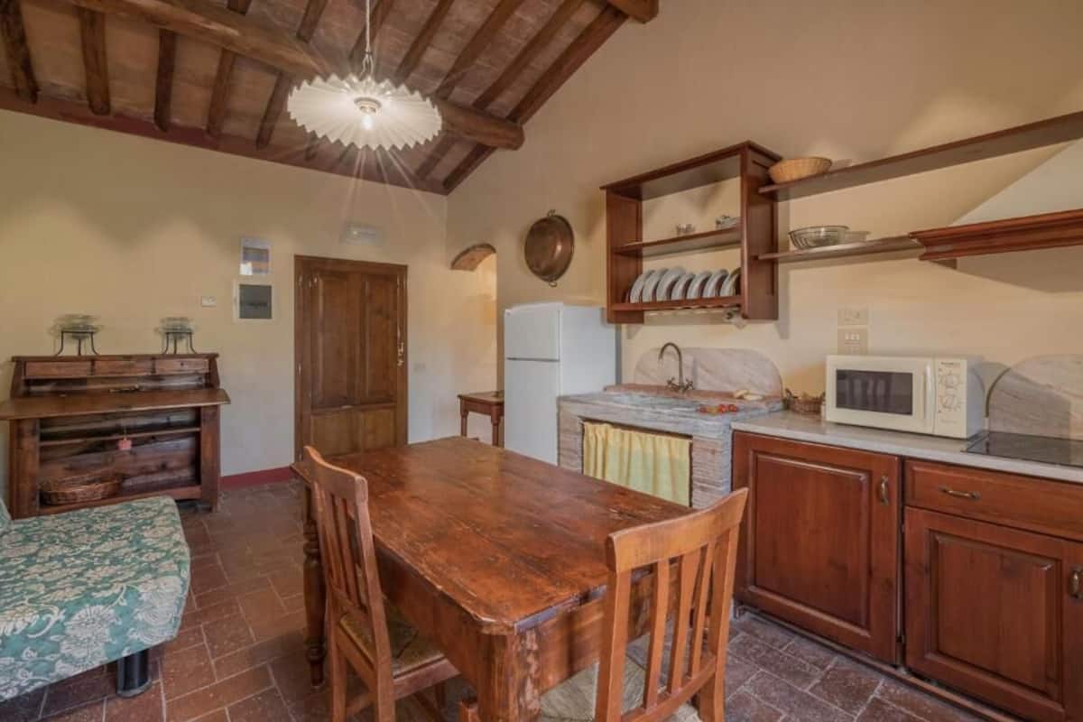 A rustic kitchen with wooden furniture, a stone fireplace, and a wooden ceiling.