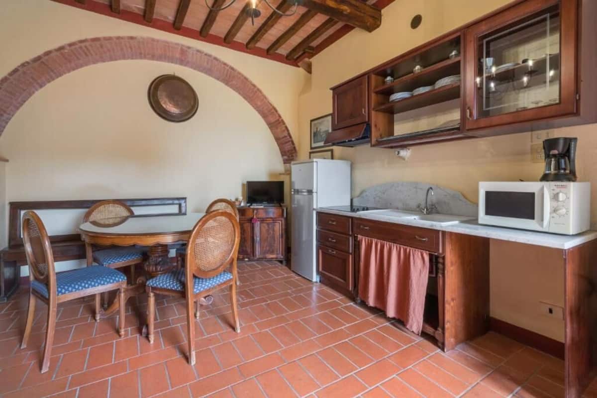 A kitchen with a dining table, chairs, a refrigerator, a microwave, and wooden cabinets.