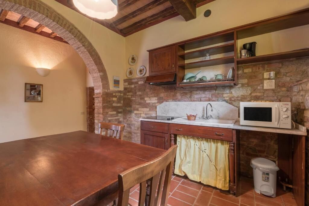 A kitchen with a stone wall, wooden cabinets, a white microwave, and a tiled floor.