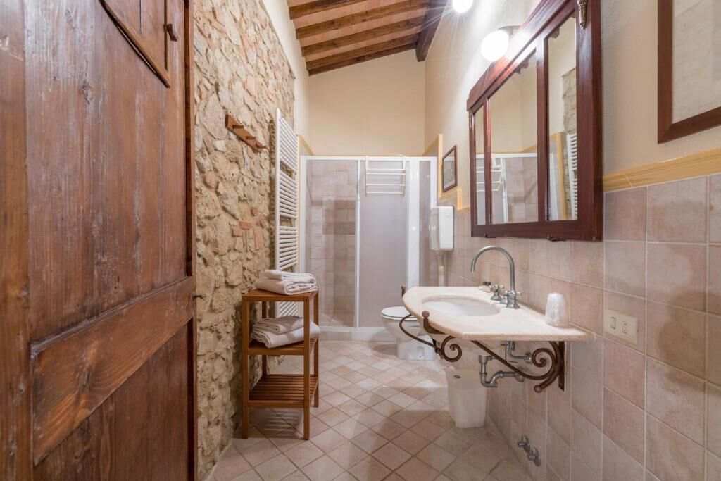 A bathroom with a stone wall, wooden door, tiled floor, a sink with a mirror, and a shower area.