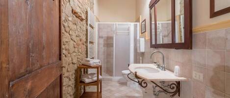 A bathroom with a stone wall, wooden door, tiled floor, a sink with a mirror, and a shower area.