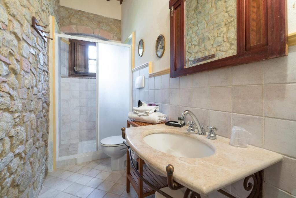 A bathroom with a stone wall, a wooden vanity, a sink, a toilet, and a shower.