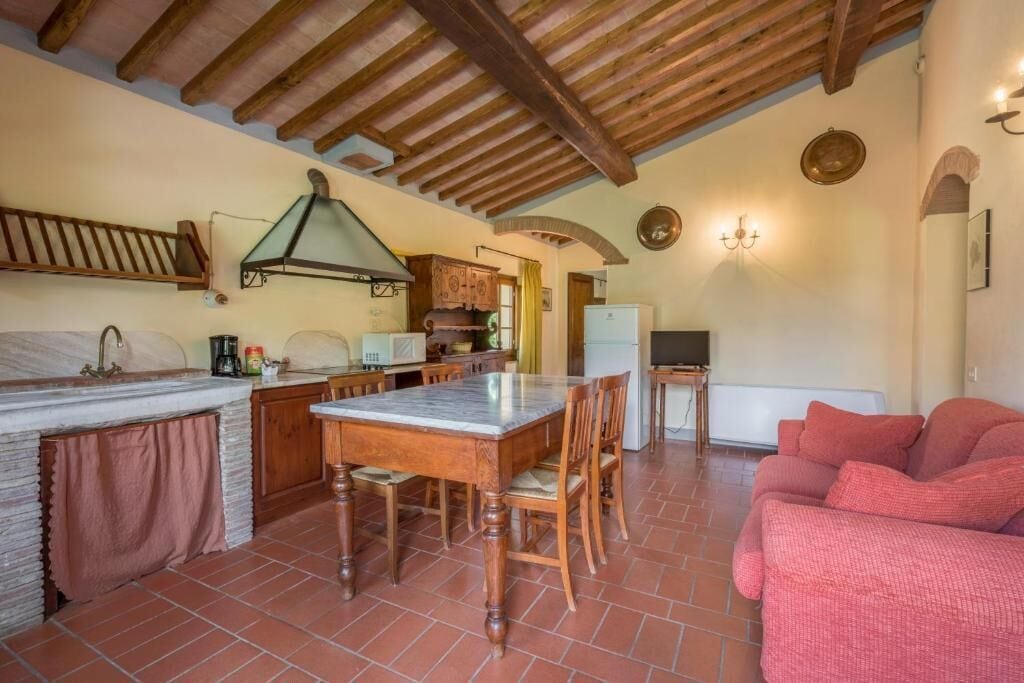 Une cuisine avec un plan de travail en marbre, des meubles en bois, une table à manger avec des chaises, un canapé rouge et un sol carrelé.