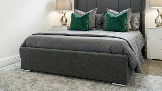 Un dormitorio con una cama tapizada en gris, mesitas de noche a juego y una alfombra gris.