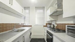 A compact kitchen with a sink, stove, microwave, and a washing machine. - Welcoming 1-bedroom apartment in the heart of London (London)