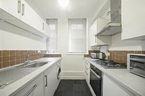 A compact kitchen with a sink, stove, microwave, and a washing machine. - Welcoming 1-bedroom apartment in the heart of London (London)