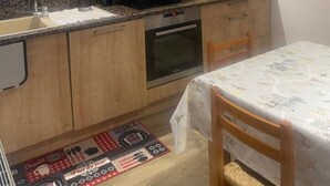 A compact kitchen with wooden cabinets, a built-in microwave, and a small dining area with a table and chairs. - Family cocoon for nature lovers overlooking the forest. (Occitanie)