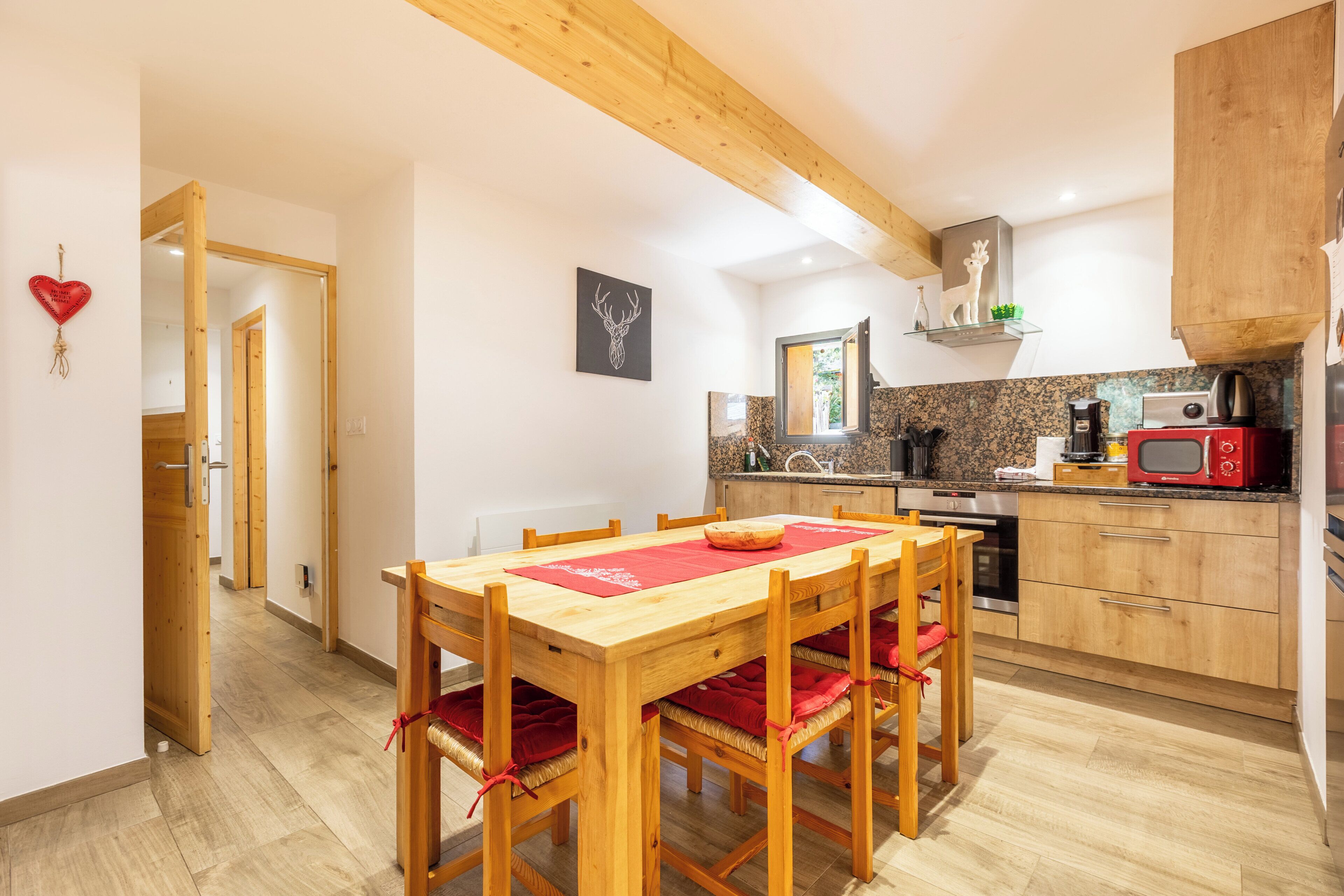 Une cuisine moderne avec des meubles en bois, un micro-ondes rouge et un coin repas comprenant une table et des chaises en bois.