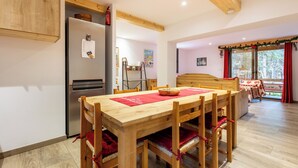 A modern kitchen with a built-in refrigerator, wooden dining table with chairs, and a cozy seating area with a bed. - Family cocoon for nature lovers overlooking the forest. (Occitanie)