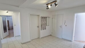 Una habitación amplia con suelo de baldosas blancas, un aplique de techo y puertas blancas.