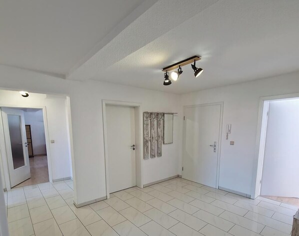 En rummelig stue med hvide flisegulve, en loftlampe og hvide døre.