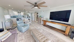 Ein modernes Wohnzimmer mit großem Fernseher, Deckenventilator und einer gemütlichen Sitzecke.