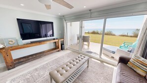 Ein Wohnzimmer mit einem großen Fernseher, einer hölzernen Sitzbank, einer gepolsterten Bank und Blick ins Freie.