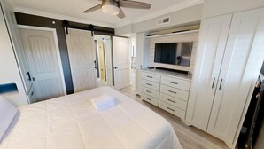 Ein Schlafzimmer mit einem Bett, einem an der Wand montierten Fernseher und einem Deckenventilator.