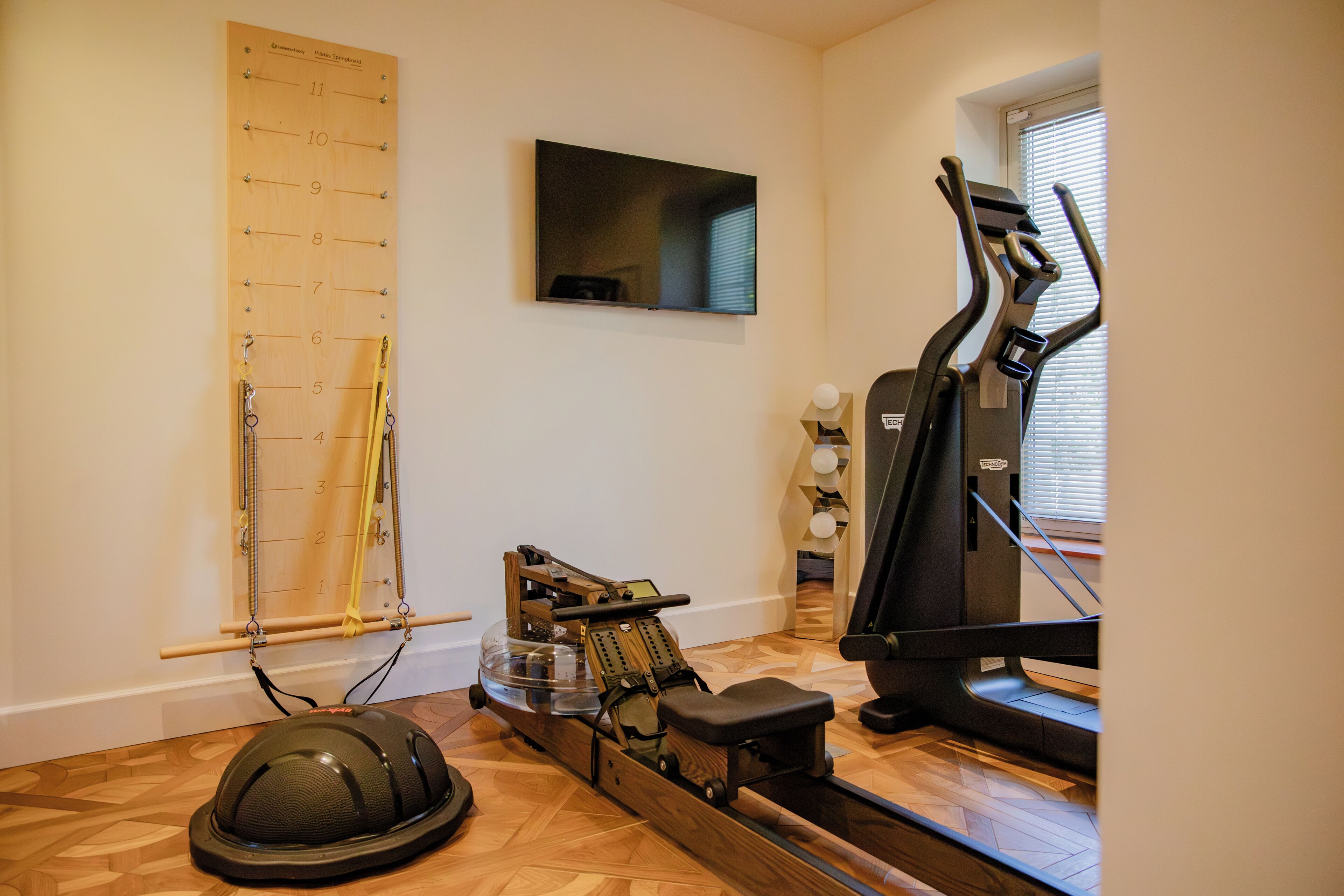 A home gym with a rowing machine, a treadmill, and a wall-mounted exercise chart.