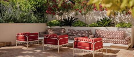 An outdoor seating area with metal furniture and patterned cushions, surrounded by lush greenery and flowering plants.