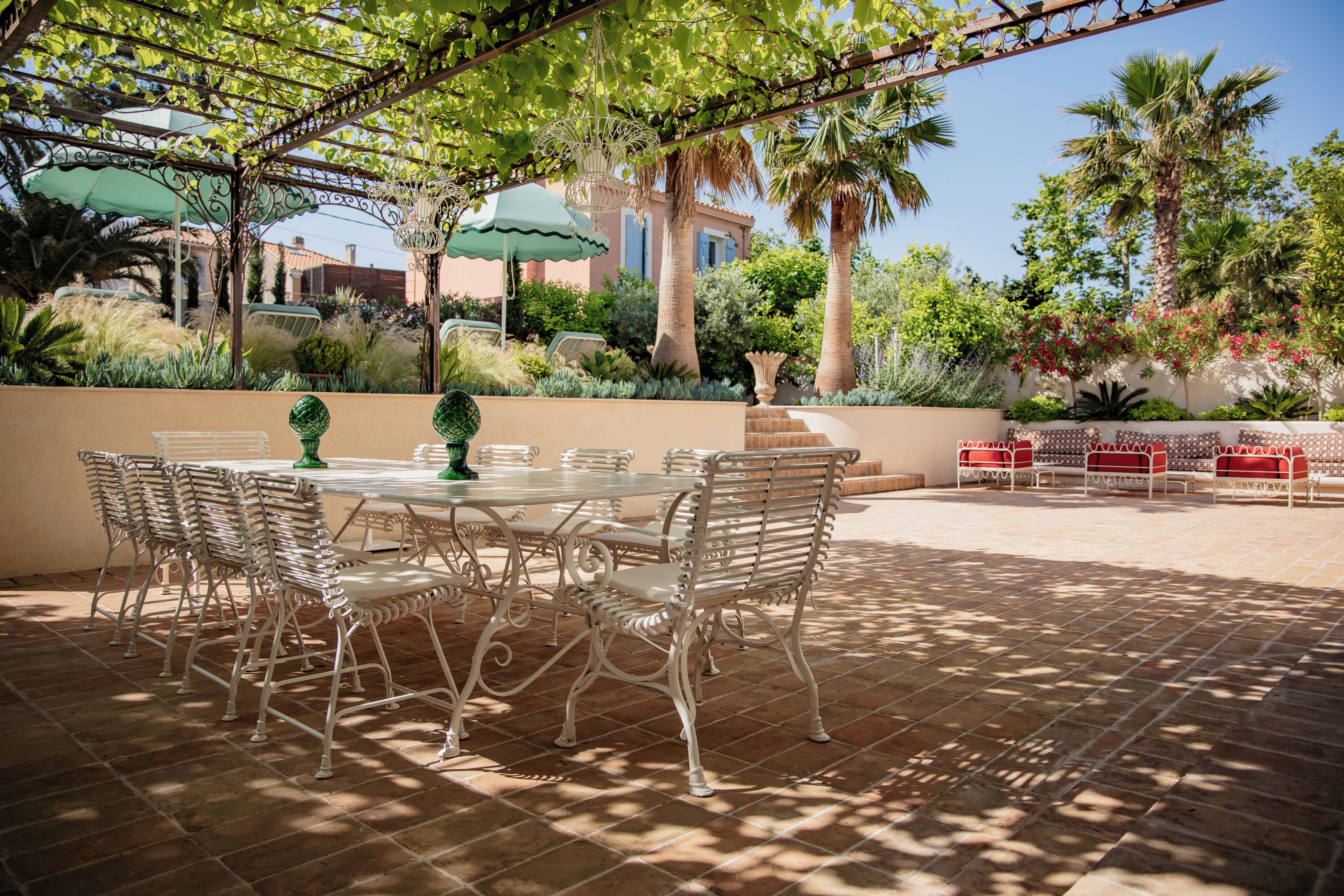 An outdoor patio with a round table and chairs, surrounded by palm trees and a pergola.