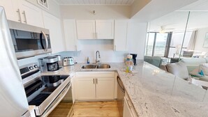 A modern kitchen with stainless steel appliances, a built-in oven, and a microwave. There is a sink with a faucet, and a coffee maker on the counter. The kitchen has white cabinets and a granite countertop. - Beautiful Inside and Out Mainsail 276 (Miramar Beach)