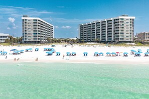 A beachfront hotel with multiple balconies, a sandy beach, and clear turquoise waters. - Beautiful Inside and Out Mainsail 276 (Miramar Beach)