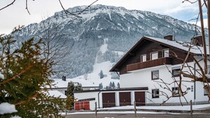 A mountain cabin with a wooden exterior, a garage, and a view of snow-covered mountains. - Apartment 'Haus Bergliebe – Zugspitzblick' with Mountain View, Balcony and Wi-Fi (Pfronten)