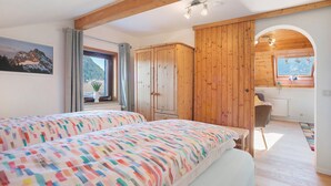 A bedroom with two beds, wooden walls, a window with a view, and a bathroom visible through an archway. - Apartment 'Haus Bergliebe – Zugspitzblick' with Mountain View, Balcony and Wi-Fi (Pfronten)