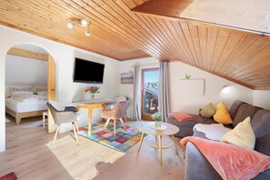A cozy room with a bed, a TV, a dining area, and a couch with pillows. - Apartment 'Haus Bergliebe - Zugspitzblick' with Mountain View, Balcony and Wi-Fi (Pfronten)