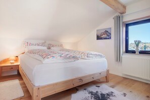 A bedroom with a wooden bed, a nightstand with a lamp, a window with a view, and a cowhide rug. - Apartment 'Haus Bergliebe - Zugspitzblick' with Mountain View, Balcony and Wi-Fi (Pfronten)