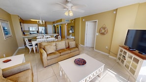 A living room with a sofa, coffee table, TV, and a dining area with chairs and a table. - Spacious Island Princess 607 w/Seasonal Beach Service (Fort Walton Beach)