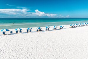 A beach with rows of blue and white beach umbrellas and lounge chairs. - Spacious Island Princess 607 w/Seasonal Beach Service (Fort Walton Beach)