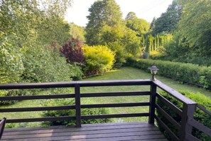 A wooden deck with a railing overlooking a well-maintained garden with various shrubs and trees.