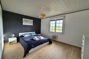 A bedroom with a bed, a nightstand, a lamp, a window, and a wall art piece. - Terraced Country House near Sea (Plurien)