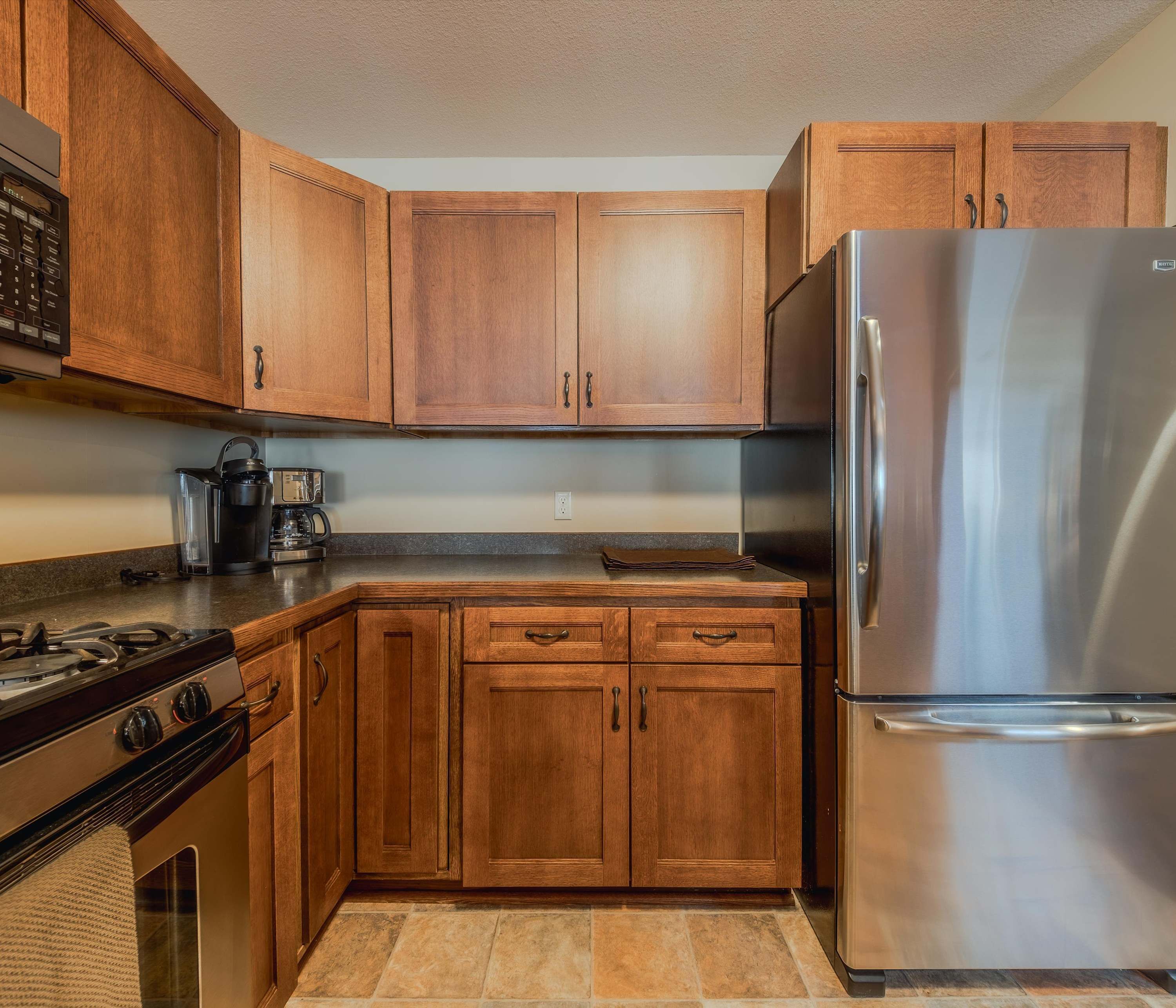 Una cocina con armarios de madera, un refrigerador de acero inoxidable, una estufa a gas y una cafetera.