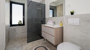 Een moderne badkamer met een douchecabine van glas, een wastafel met spiegel en een toilet.
