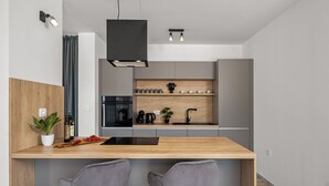 Een moderne keuken met een houten aanrecht, twee grijze barkrukken, een zwart hanglamp en een inbouwkastje met keukengerei.