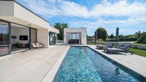 Een modern buitenzwembadgedeelte met een heldere lucht, een zwembad, ligbedden en een zitgedeelte met een tafel en stoelen.