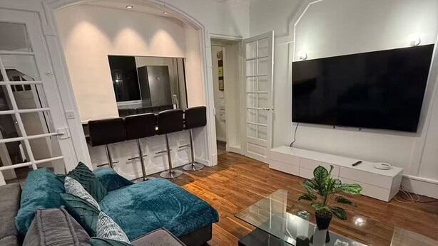 Un salon moderne doté d’un grand téléviseur à écran plat, d’une table basse en verre et d’un canapé agrémenté de coussins à motifs.
