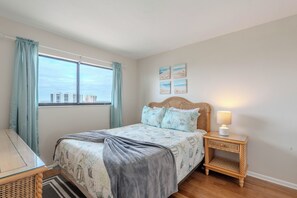A bedroom with a bed, a bedside table with a lamp, a window with curtains, and wall art. - 🌊Beachfront with Great Gulf Views | Easy Beach Access | Carlos Pointe #624⛱️ (Fort Myers Beach)