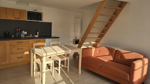 A compact kitchen with wooden cabinets, a dining table with chairs, a sofa, and a wooden staircase. - Gîte de Vouhé near Surgères apartment 2 (Vouhé)