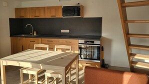A modern kitchen with wooden cabinets, a black countertop, a microwave, an oven, and a dining area with a table and chairs. - Gîte de Vouhé near Surgères apartment 2 (Vouhé)