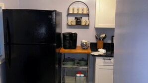 Een kleine keuken met een zwarte koelkast, een koffiezetapparaat en een plank met mokken.