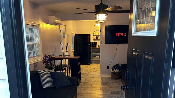 Een moderne woonkamer met een donkere bank, een eethoek en een keuken op de achtergrond.