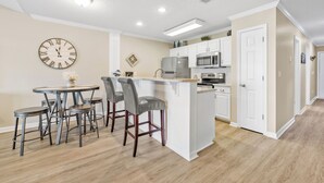 Una cocina moderna con armarios blancos, una isla central, taburetes de bar y un reloj en la pared.