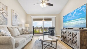 Una sala de estar con sofá, mesa de centro, televisor y vistas al exterior.