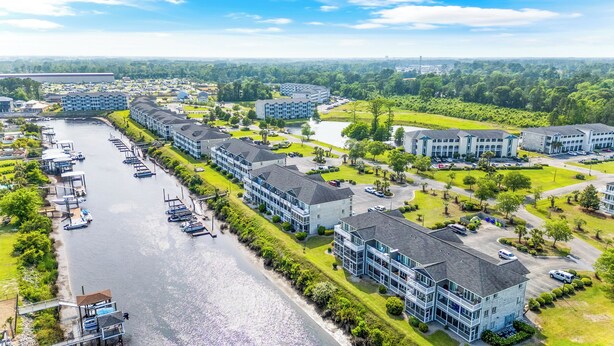Un hotel frente al agua con varias construcciones, un puerto deportivo con barcos y abundante vegetación.