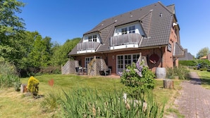 A two-story house with a brick exterior, a tiled roof, and a front porch with outdoor furniture. - Ferienwohnung mit Balkon in St.peter-ording (St. Peter-Ording)