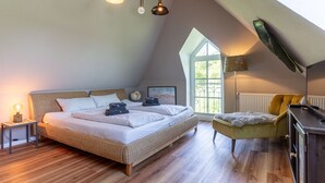 A bedroom with a large bed, a nightstand, a desk, a chair, and a window with a view of greenery. - Ferienwohnung mit Balkon in St.peter-ording (St. Peter-Ording)